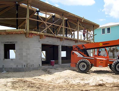 Hurricane-Resistant Elevated Beach House: Concrete Block Foundation with Flood Vents for Storm Surge Protection Elevated hurricane-proof beach house construction with reinforced concrete block foundation and flood vents for floodwater flow, featuring telescopic handler and open garage level on sandy coastal site.