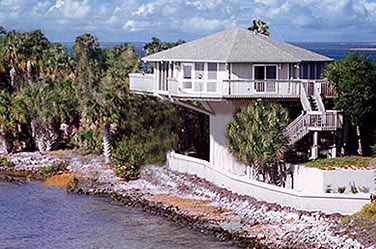 Topsider Hurricane-Proof Pedestal Home in Coastal Florida: Survived Years of Hurricanes, Tropical Storms, and Storm Surge with Unrivaled Strength and Luxury Topsider hurricane-resistant coastal Florida pedestal home surviving storm surge and waves during tropical storm or hurricane, elevated design for flood and wind protection with lush palm trees, oceanfront views, and sturdy construction.
